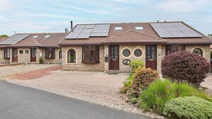 Une rangée de maisons à deux étages, dotées de panneaux solaires sur les toits, de murs en pierre et d’une allée pavée.