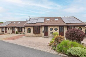 A row of two-story houses with solar panels on the roofs, stone walls, and a paved driveway. - Host & Stay | Puffin Cove (Seahouses)