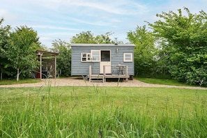 Une petite cabane à un seul étage, dotée d’un porche, entourée d’un champ herbeux et d’arbres.