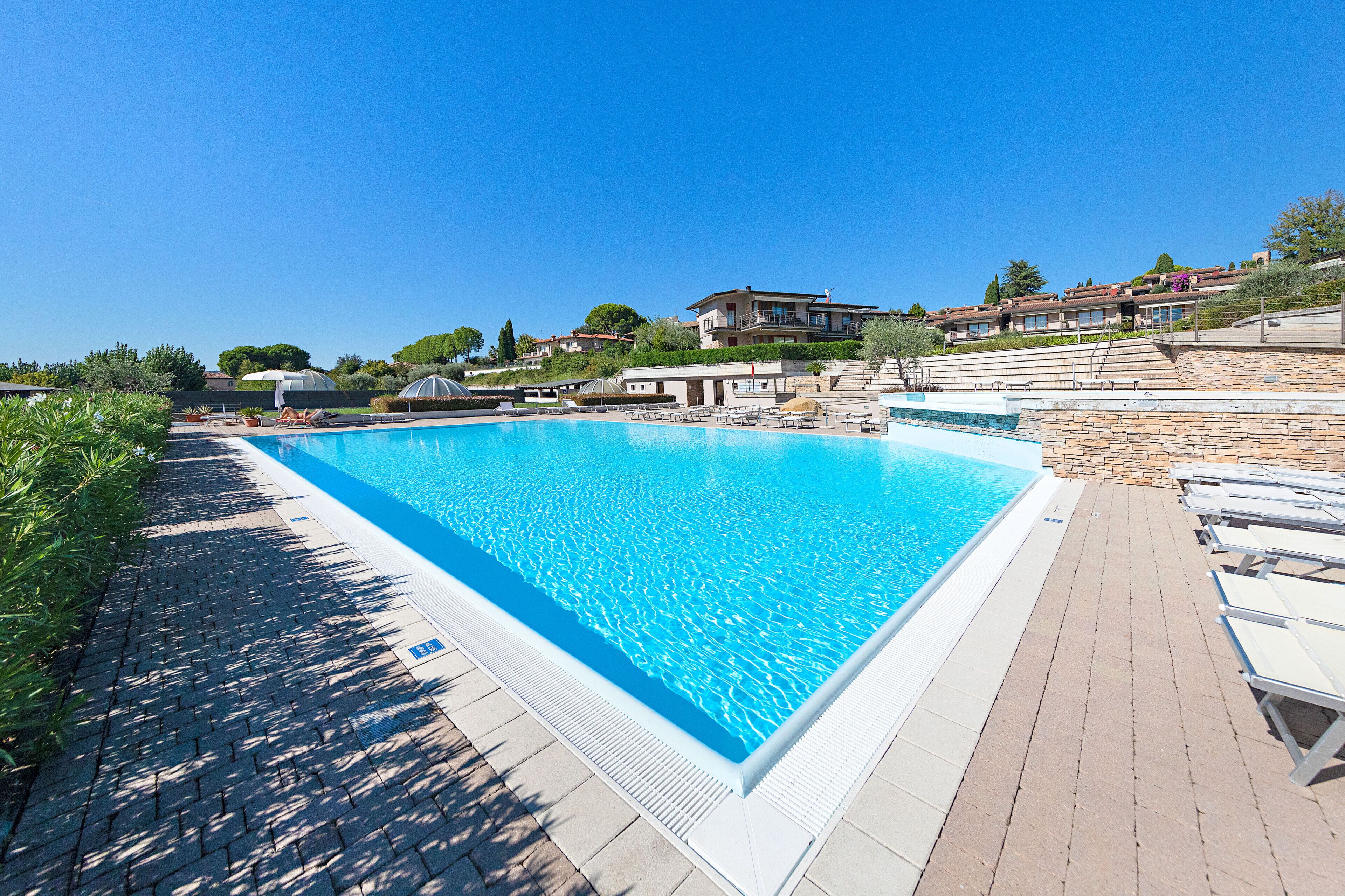 A rectangular swimming pool with a clear blue water surface, surrounded by a paved deck with lounge chairs.