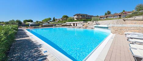 A rectangular swimming pool with a clear blue water surface, surrounded by a paved deck with lounge chairs.