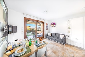 Ein Essbereich mit Tisch, gedeckt für eine Mahlzeit, einer Couch und einem an der Wand befestigten Fernseher.