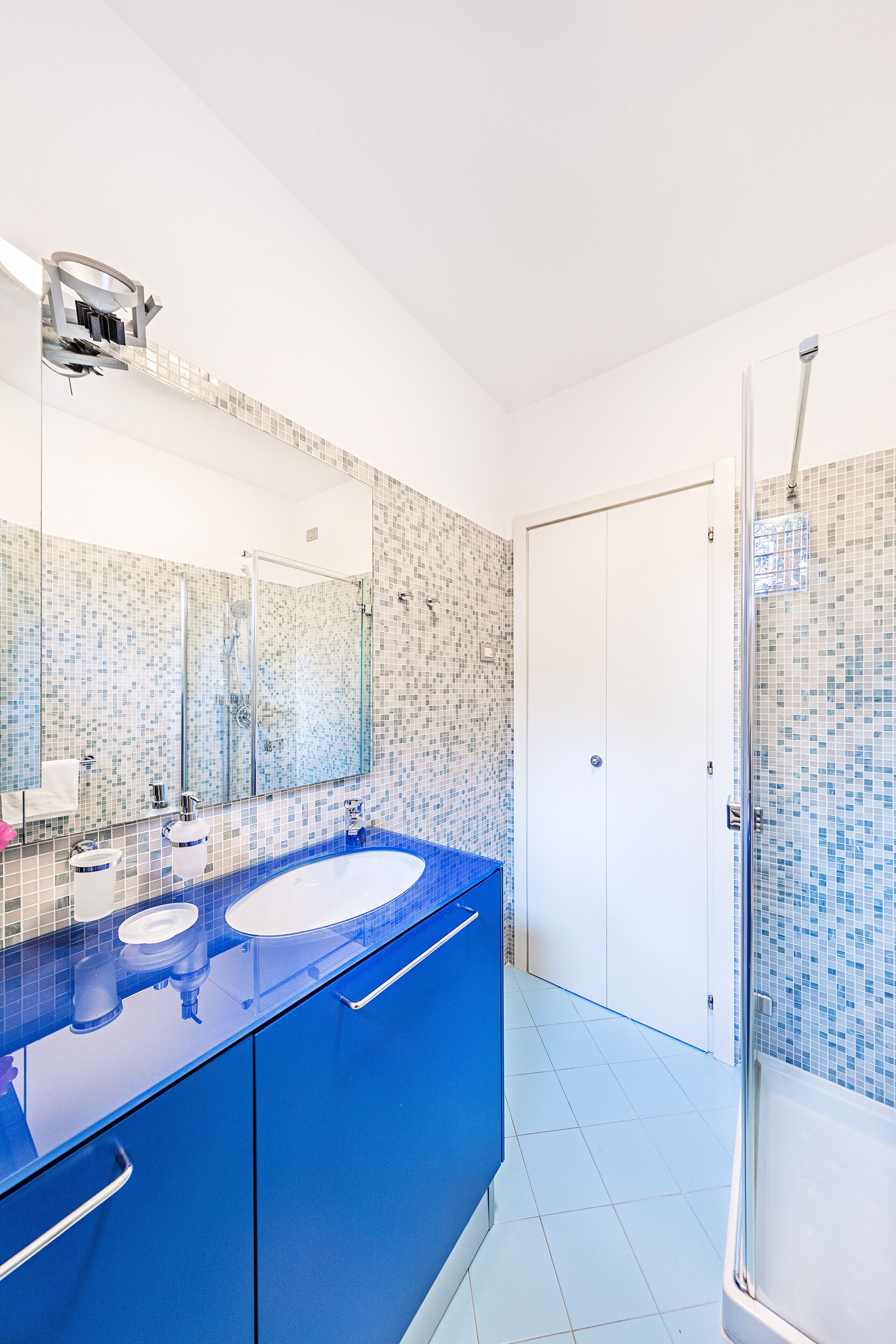 Une salle de bain avec un meuble-lavabo bleu, un grand miroir, une douche et un sol carrelé.