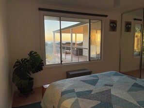 A bedroom with a large window, a bed, a potted plant, and a view of the outside.
