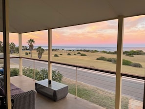 A covered outdoor seating area with a view of the ocean and a sunset.