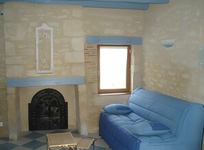 A room with a stone wall, a window, a blue sofa, and a fireplace. - Charming Restored Small Barn (Montignac-Lascaux)