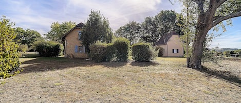 A rural property with two stone houses, a grassy field, and mature trees.