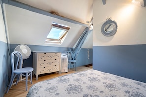 A bedroom with a sloped ceiling, a skylight, a dresser, a chair, a fan, and a patterned rug. - Charming Restored Small Barn (Montignac-Lascaux)