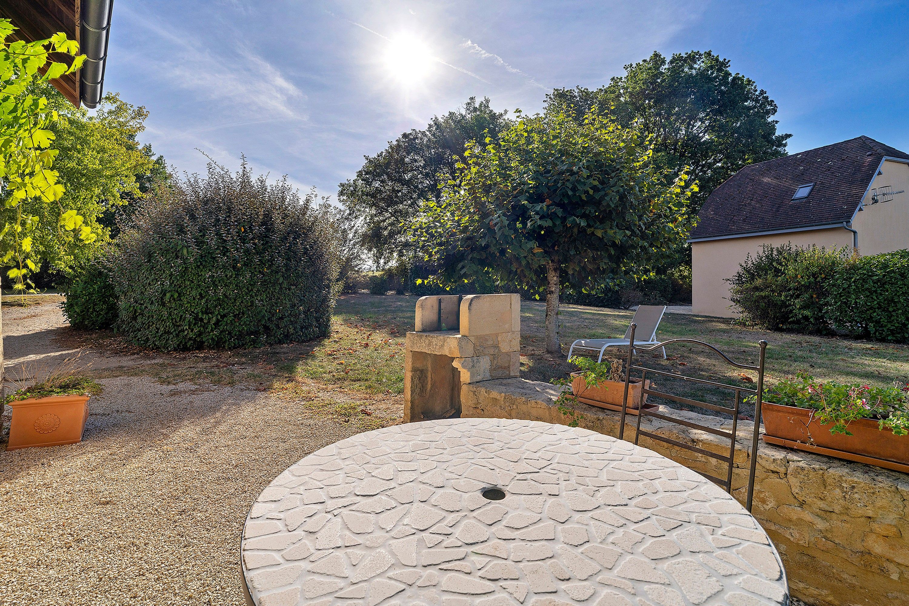 Een tuin met een stenen tafel, een metalen hek en een gebouw op de achtergrond.