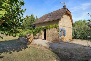 A stone building with a tiled roof, a gravel driveway, and a small garden area. - Charming Restored Small Barn (Montignac-Lascaux)