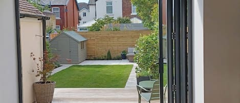 A view through an open door into a backyard with a wooden deck, a small shed, and a lawn.