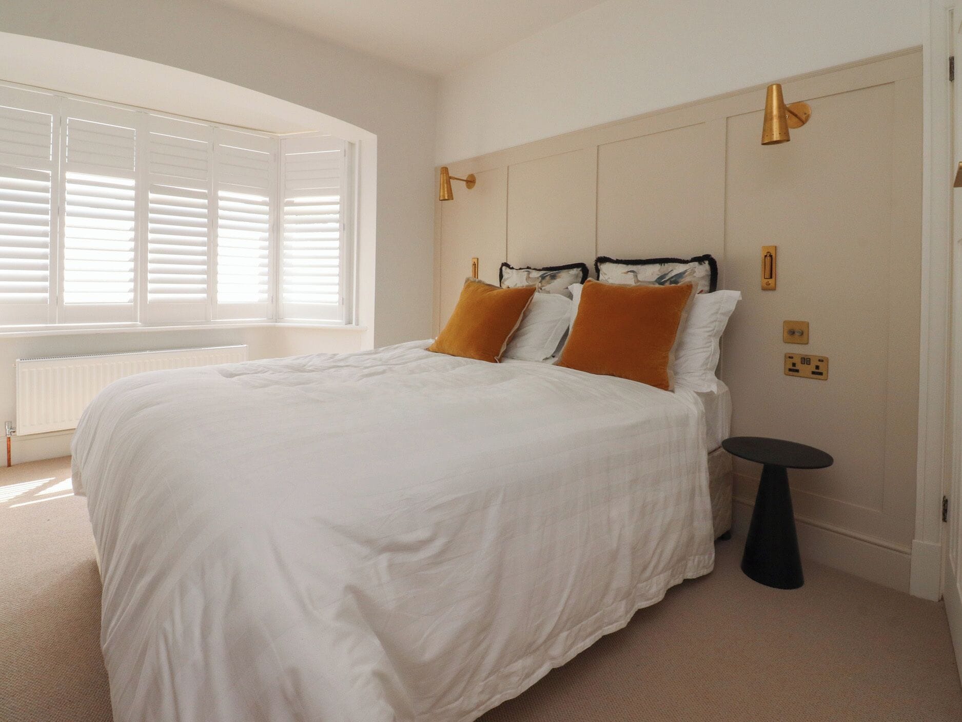 A bedroom with a bed, white bedding, a small round table, and a window with blinds.