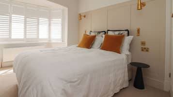 A bedroom with a bed, white bedding, a small round table, and a window with blinds.