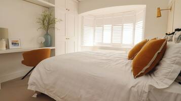A bedroom with a bed, a desk, a chair, a window with blinds, and a plant.