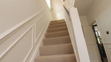 A staircase with beige carpeted steps, white walls, and a white railing.