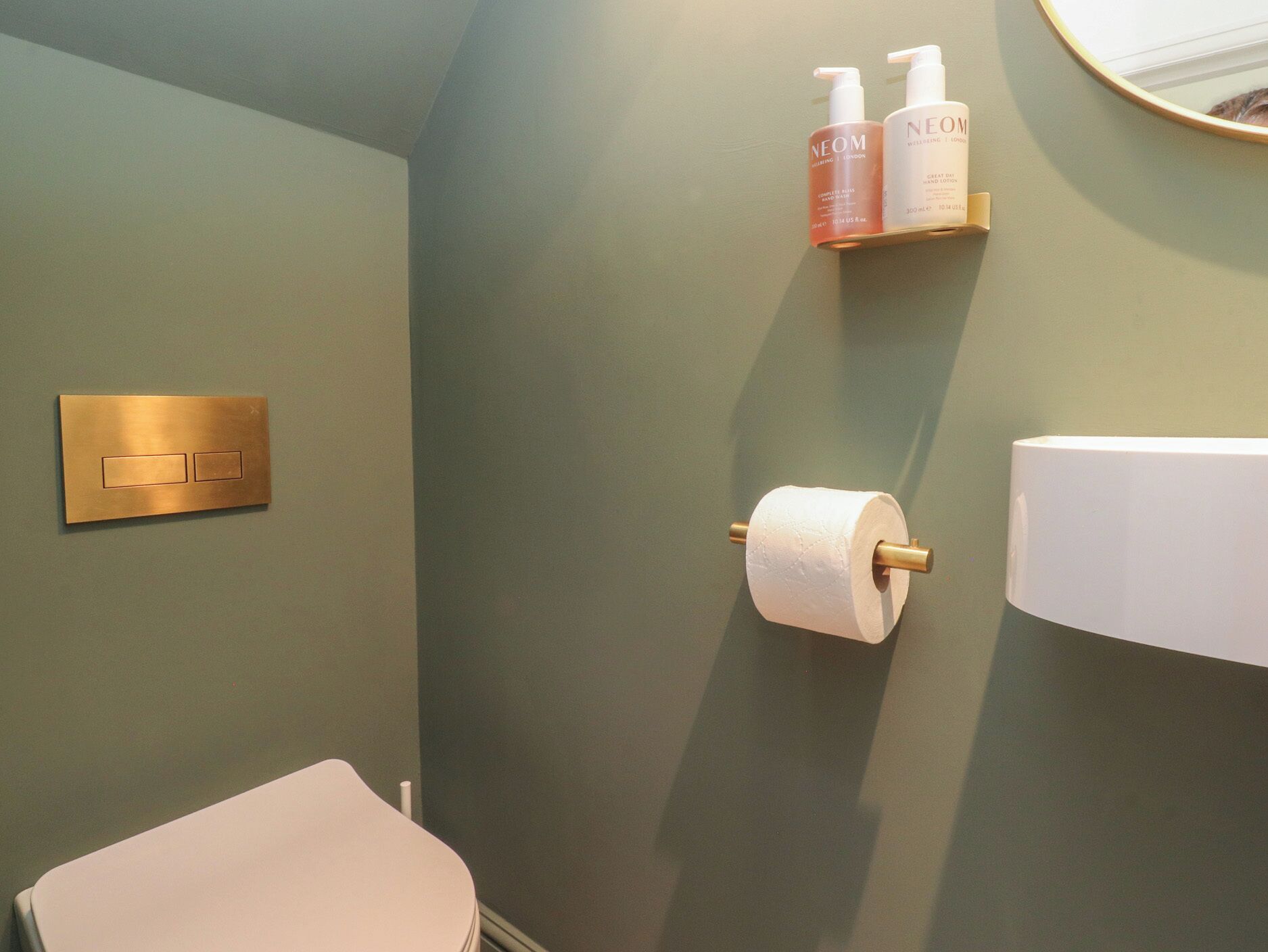 A bathroom with a toilet, a wall-mounted toilet paper holder, and two toiletry bottles on a shelf.