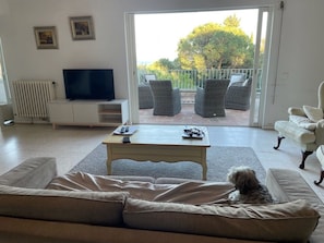Ein Wohnzimmer mit einer Couch, einem Couchtisch, einem Fernseher und einem Balkon mit Korbstühlen.