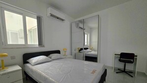 A bedroom with a bed, bedside tables, a desk, a chair, a mirror, and an air conditioning unit. - 3 bedroom, 2 bathroom Brand new Apartment in Central Gozo (Ir-Rabat Għawdex)