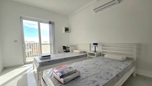 A bedroom with two beds, a small desk, a chair, a nightstand, and a window with a view. - 3 bedroom, 2 bathroom Brand new Apartment in Central Gozo (Ir-Rabat Għawdex)