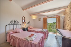 A bedroom with two beds, a wooden wardrobe, a mirror, and a balcony with a view.