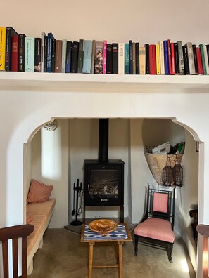 Een knus hoekje om in te lezen, met een boekenkast, een open haard, een comfortabele bank en een klein tafeltje met een decoratieve schaal.
