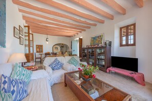 A living room with a sofa, coffee table, and a television. There is a bookshelf and a painting on the wall.