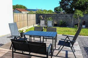 An outdoor patio with a table and chairs, surrounded by a wooden deck and a stone wall. - Air-conditioned, comfortable new house, ideal for families and friends. (Biscarrosse)