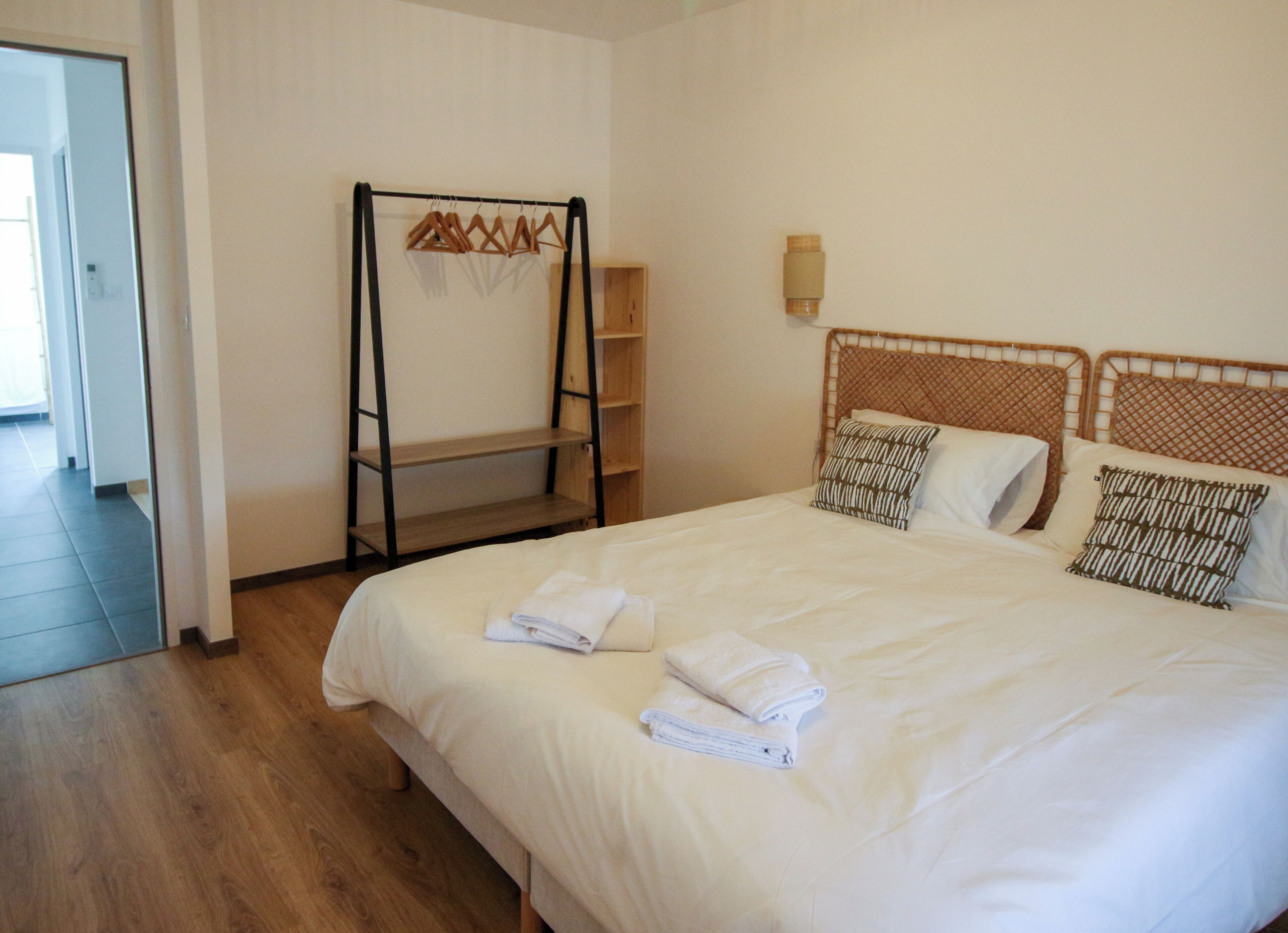 A hotel room with a large bed, a wooden wardrobe, a towel rack, and a wooden floor.