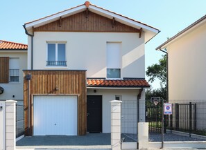 Een tweelaags huis met een witte gevel, een houten veranda en een pannendak.