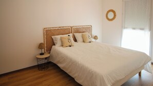Un dormitorio con cama, una mesita redonda, una lámpara y una ventana con persianas.