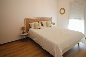 Een slaapkamer met een bed, een rond nachtkastje, een lamp en een raam met zonwering.