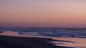 Una playa con olas, cielo despejado y algunas personas caminando.