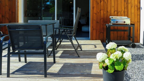 Un patio al aire libre con una mesa y sillas, una planta en maceta y un ventanal corredera que da a un espacio interior.