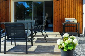 Um pátio externo com mesa e cadeiras, uma planta em vaso e uma porta de vidro deslizante que dá para um espaço interno.