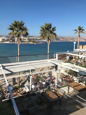 Eine Dachterrasse mit Sitzgelegenheiten im Freien, Palmen und Meerblick.