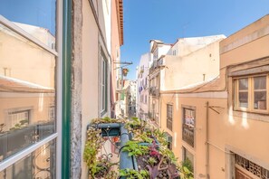 A narrow urban street with buildings on either side, a visible balcony with plants, and a clear blue sky. - Historic & Typical 1 By Gt House (Lisbon)