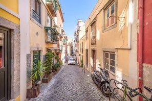 A narrow cobblestone street flanked by buildings with balconies, a parked motorcycle, and a car in the distance. - Historic & Typical 1 By Gt House (Lisbon)