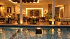Uma área na piscina com uma mesa redonda, cadeiras e um espaço de refeições ao fundo.