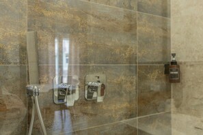 A shower area with a glass door, a handheld showerhead, and a soap dispenser on the wall.