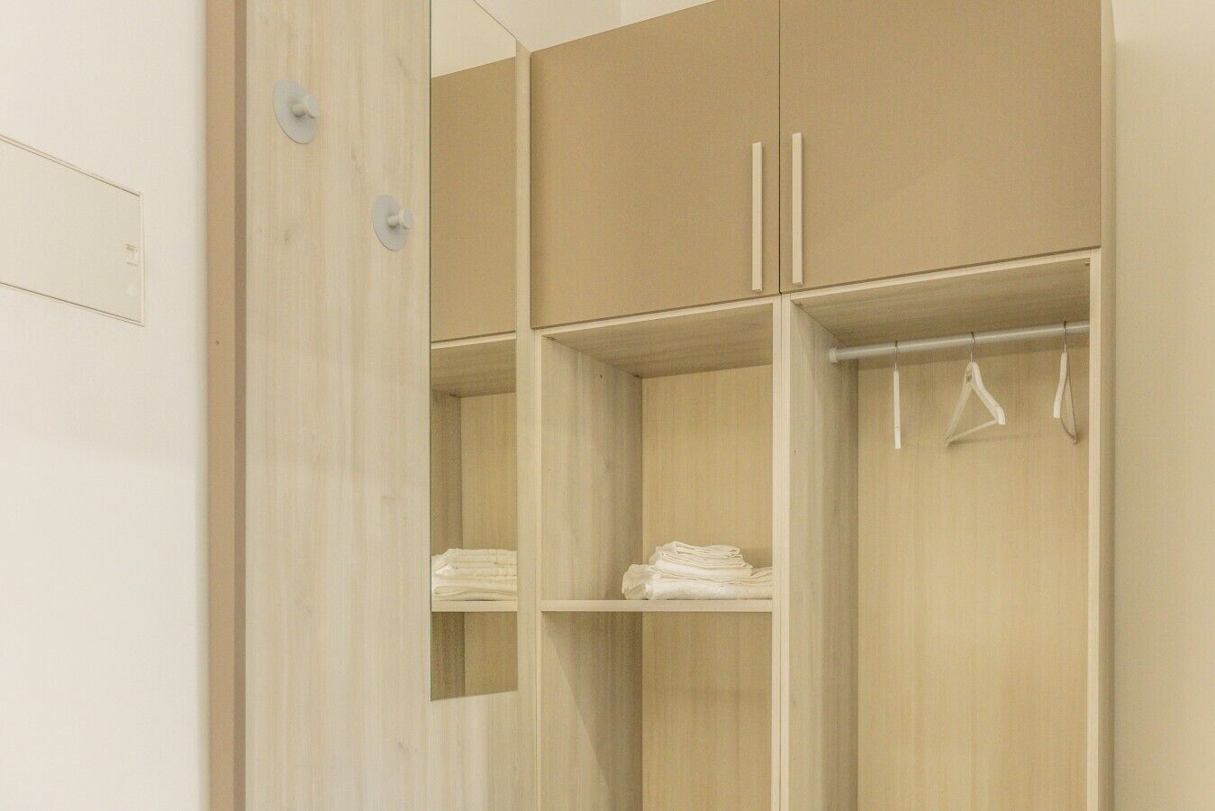 Een houten garderobe met twee deuren, een kledingstang en een spiegel.