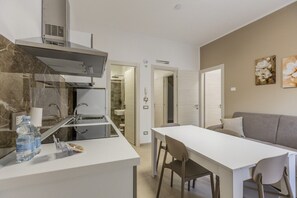A compact kitchen with a built-in stove, a dining area with a table and chairs, and a grey sofa.