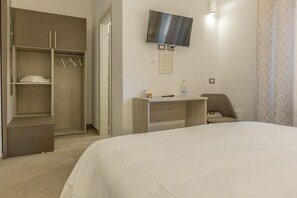 A hotel room with a bed, a desk, a chair, a TV, and a wardrobe.