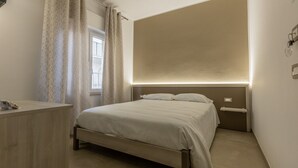 A bedroom with a bed, bedside tables, a desk, and a window with curtains. - Nova Suite - Apartment 200 (Calatafimi)