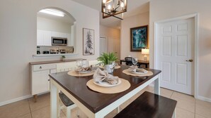 A dining area with a long table, white cabinets, a microwave, and a chandelier. - WP301 - 3BR Condo Near Walt Disney World (Kissimmee)