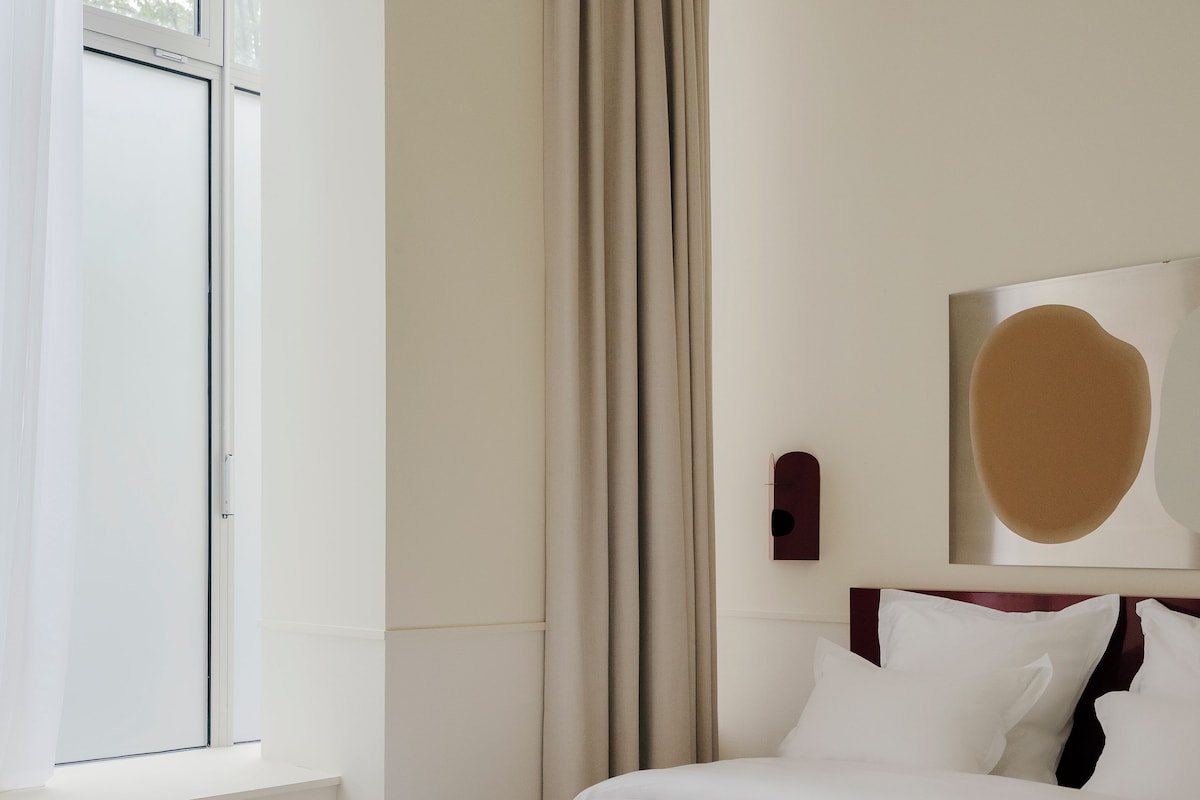 A neatly arranged hotel room with a bed, a window, and a wall-mounted artwork.