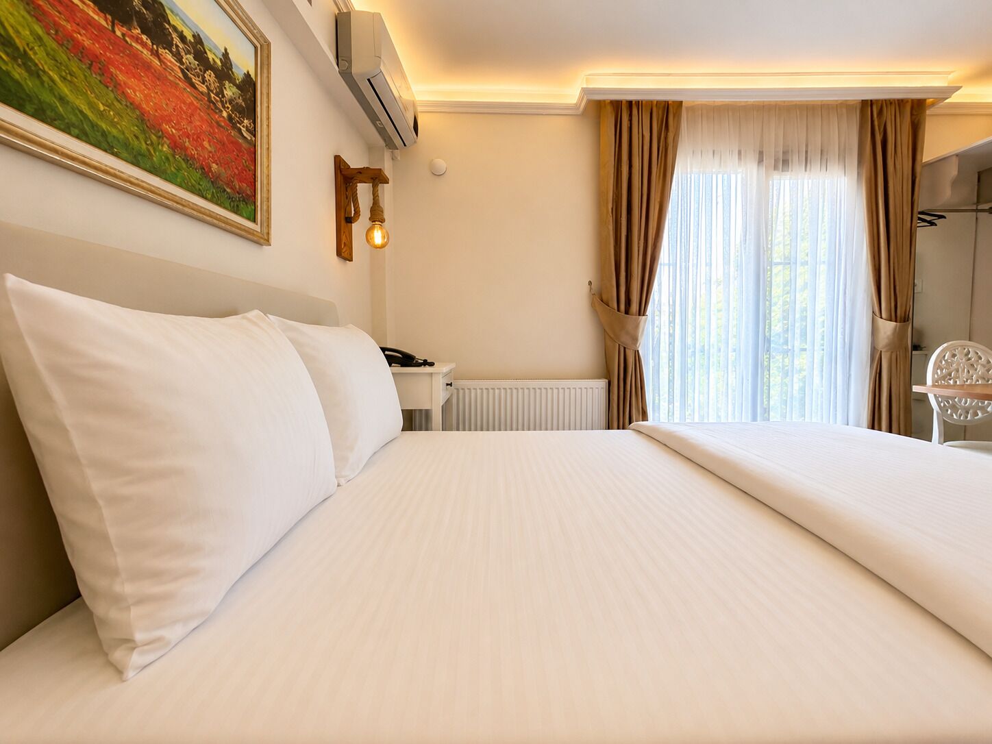 A hotel room with a large bed, a bedside table with a lamp, a radiator, and a window with curtains.