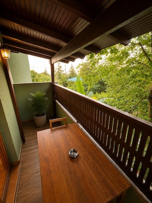 Una mesa de madera con un cuenco de metal, una planta en maceta y vistas a la vegetación a través de una cerca de madera.