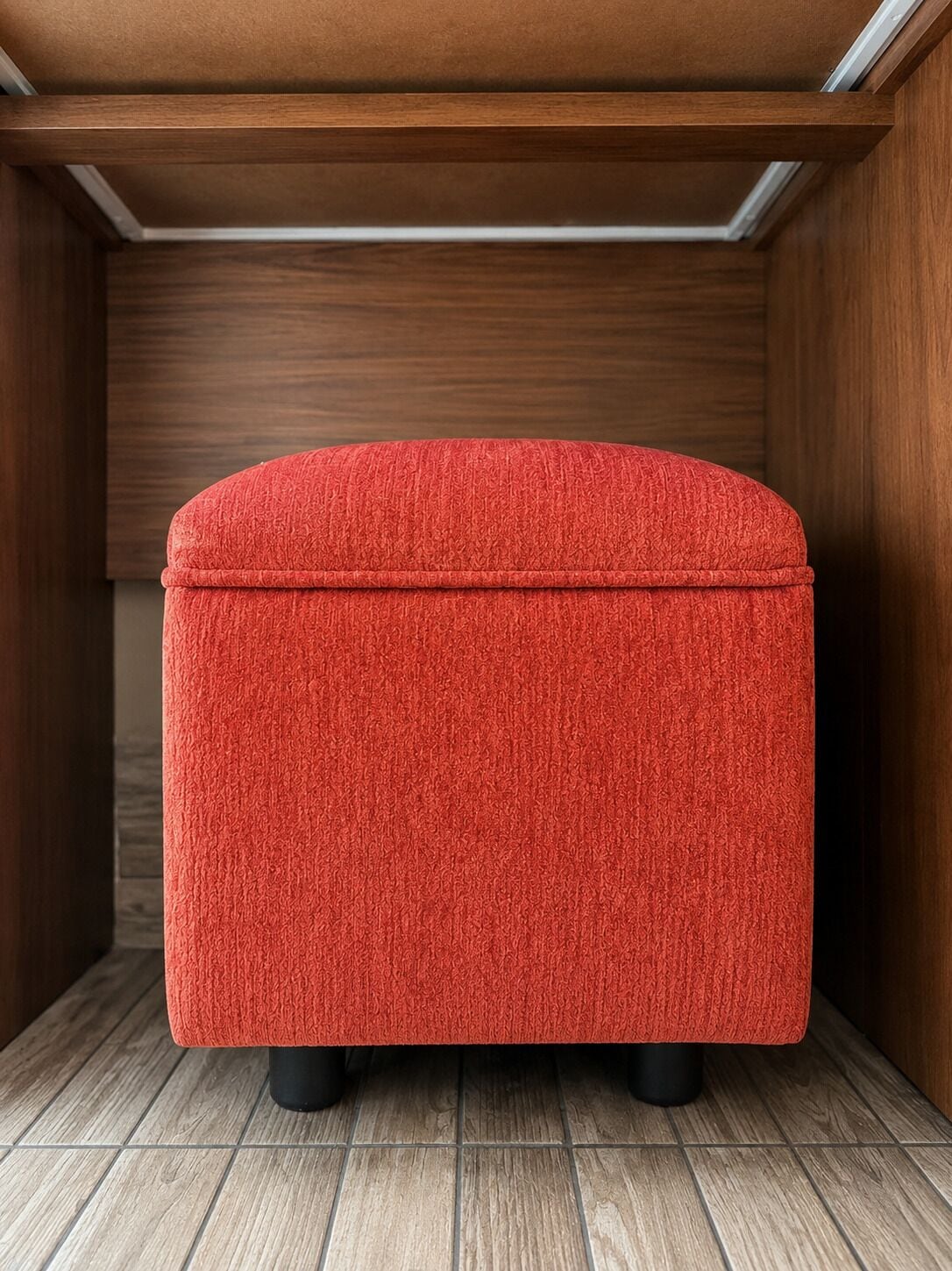 Un otoman rojo en una habitación de madera con techo inclinado y paredes de madera.
