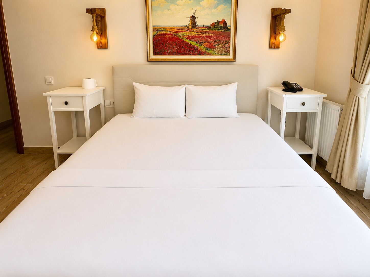 A neatly made bed with white linens, two bedside tables with lamps, a painting above the bed, and a radiator on the wall.