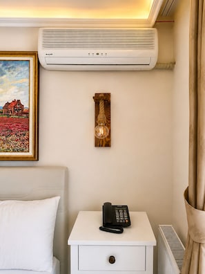 A hotel room with a bed, a bedside table with a phone, a wall-mounted air conditioner, and a framed painting. - Motto Hotel Polonezköy (Beykoz)